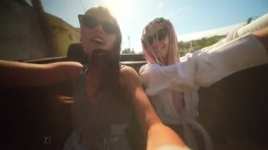 İki iyi arkadaş neşeli bir şekilde üstü açık bir arabada güneşli bir yolculuğun tadını çıkarıyorlar. Birlikte güzel anları yakalıyorlar.