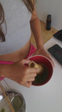 Bir kadın aktif olarak bir kasede kibrit çayı çırpıyor ve geleneksel Japon çay hazırlama sanatını sergiliyor.