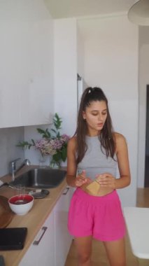 Genç bir kadın parlak bir mutfakta neşeli bir şekilde yemek pişiriyor, canlı renkler sergiliyor ve büyüleyici, sıradan bir tarzı var.