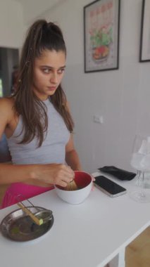 Genç bir kadın, parlak ve modern bir mutfakta canlı bir kibrit yeşil çay hazırlıyor.