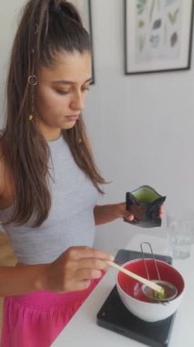 Genç bir kadın, şık mutfağında canlı dekorlarla dolu geleneksel aletlerle matcha çayı hazırlıyor.