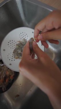 İki yetenekli el, lavaboda kevgire batırılmış taze karidesi titizlikle temizler ve lezzetli bir yemeğe hazırlanır.