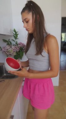 Gündelik giysiler içindeki genç bir kadın, parlak, renkli mutfağında zevkle yemek pişirir ve temizlik yapar.