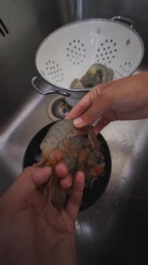 Mutfak lavabosunda taze karidesleri özenle yıkayan bir insan, onları lezzetli bir yemek düzenine hazırlar.