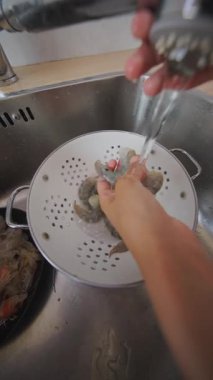 Bir birey taze karidesleri lavaboda yıkıyor, deniz ürünleri hazırlama teknikleri ve yöntemlerine odaklanıyor.