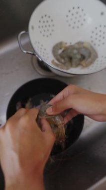 Bir insan karidesleri elleriyle dikkatlice temizliyor, bugün sıcak bir mutfakta yemek pişirmek için deniz ürünlerini hazırlıyor.