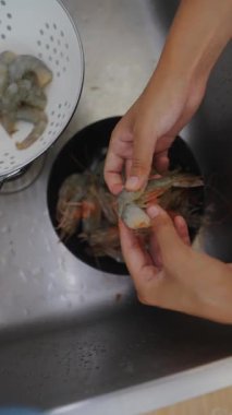 Eller, inanılmaz lezzetli bir yemek için mutfak lavabosunda karidesi özenle temizleyip dikkatlice hazırlıyor.