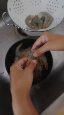 Canlı bir mutfak ortamındaki taze karidesleri temizleme ve soyma işleminin ayrıntılı adımlarına dikkat edin.