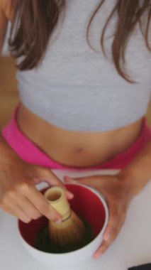 Bir insan geleneksel bambu çırpma aletini kullanarak titizlikle matcha çayı hazırlıyor.