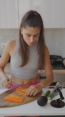 Modern bir mutfakta taze havuç doğrayan genç bir kadın sağlıklı beslenmenin önemini vurguluyor.