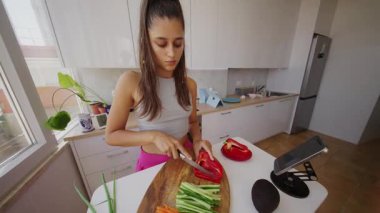 Genç bir kadın parlak ve modern bir mutfakta çeşitli taze sebzeler hazırlıyor.