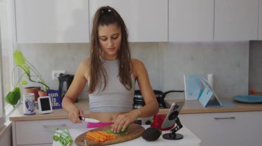 Bir kadın modern bir mutfakta taze, renkli sebzeler hazırlıyor, yemek pişirme sürecini bir vlog için filme çekiyor.