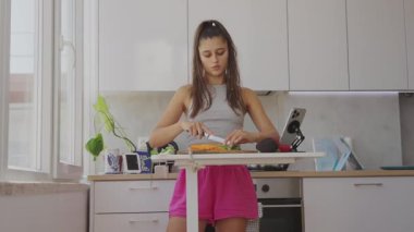 Genç bir kadın, modern, güneşli bir mutfakta sağlıklı bir yemek için taze malzemeler hazırlıyor.