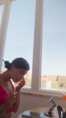 Bir kadın sabah hazırlanıyor, güzel manzaranın tadını çıkarırken makyaj yapıyor, günlük rutinini yakalıyor.