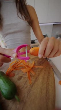 Canlı bir mutfak hazırlığında rengarenk bir sopayla taze havuç soyan birinin resmi.