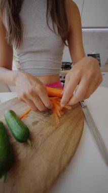 Modern bir mutfakta renkli aletlerle taze havuç ve salatalık soyma ve kesme sahnesi.