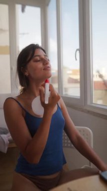 Bir kadın ferahlatıcı bir kişisel bakım rutinine dalıp aydınlık, güneşli bir ortamda dinlenmenin tadını çıkarır.