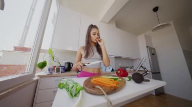 Güneşli bir mutfakta, genç bir kadın taze sebzeler hazırlıyor, sağlıklı yemek yapmanın keyfini çıkarıyor.