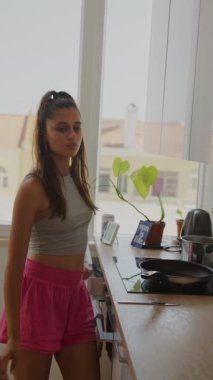 Genç bir kadın, bol doğal ışıkla dolu modern bir mutfakta yemek hazırlıyor.