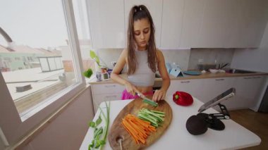 Güneşli bir mutfakta, genç bir kadın ahşap bir tahtada taze, renkli sebzeler hazırlıyor, mutfak yeteneklerini sergiliyor.