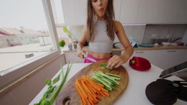 Işıl ışıl yanan bir mutfakta, genç bir kadın besleyici ve sağlıklı bir yemek için bir dizi sebze hazırlar.