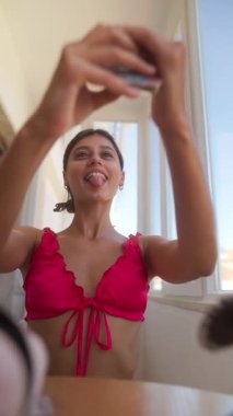 Canlı genç bir kadın, akıllı telefonuyla neşeli selfie çekerken parlak doğal ışığın tadını çıkarıyor.