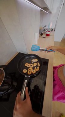 Çağdaş bir mutfak düzeninde, rengarenk spatulalarla tavada karidesi ustalıkla fırlatan bir insan..