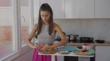 Genç bir kadın şık mutfağında lezzetli yemekler hazırlamakla meşgul, çeşitli canlı malzemeler sergiliyor.