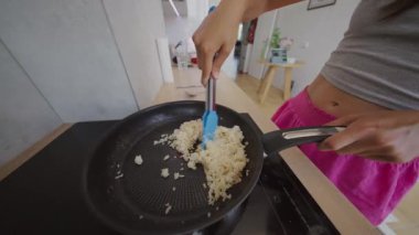 Parlak ve davetkar bir mutfakta, yetenekli bir insan mavi spatula kullanarak tavada pilav pişiriyor.