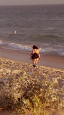 Kıyı boyunca zarif bir şekilde koşan bir kadın, nefes kesici bir gün batımı kumsalının huzurlu atmosferini kucaklıyor.