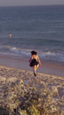 Kaygısız bir kadın, kıyı şeridi boyunca sakin bir yürüyüş yapar. Sıcak güneşin ve yumuşak okyanus esintisinin tadını çıkarır.