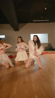 Beyaz kostümlü üç dansçı aydınlık bir stüdyoda büyüleyici bir gösteri sergiliyor, seyircileri büyülüyor.