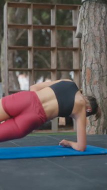 Formda bir kadın parkta yoga minderinde yan kalas yapıyor. Gücünü ve dengesini gösteriyor..