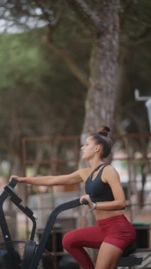 Genç bir kadın dışarıda, sakin bir ortamda spor yapıyor. Spor ve sağlık hizmetlerini destekliyor.