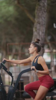 Odaklanmış genç bir kadın, sakin ve sakin bir açık hava ortamında özenle egzersiz bisikleti üzerinde çalışıyor.