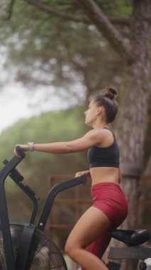 Formda genç bir kadın hava bisikleti ile doğada egzersiz yapar, sağlık ve zindeliğe bağlılığını gösterir.