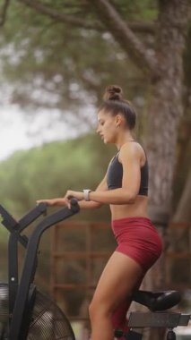 Odaklanmış bir kadın tutkulu bir şekilde egzersiz bisikletine biner ve çevresi doğal güzelliklerle çevrilidir.