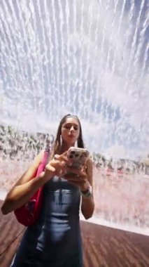 Bir insan akıllı telefonunu gün ışığında büyüleyici ve büyüleyici bir su tesisatı altında kullanmaktan zevk alır.