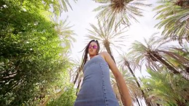 Şık bir kadın, bereketli palmiye ağaçlarının arasında güneşli bir ortamda kendine güven ve tarz yayar..