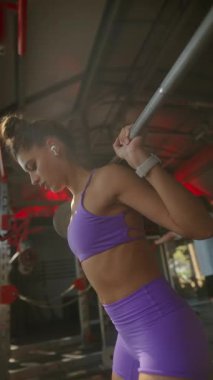 Adanmış, atletik bir kadın, enerjik, hareketli ve modaya uygun bir spor salonunda halterle çömelme hareketleri yapıyor.