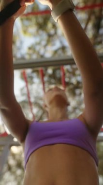 Kendini işine adamış bir sporcu, şık, mor bir giysiyle barfiks çekip, gücünü ve dikkatini topluyor..