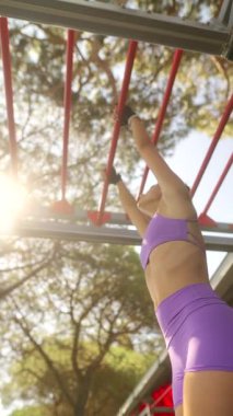 Kendini adamış bir fitness meraklısı enerjik bir şekilde canlı güneş ışığı altında maymun parmaklıkları üzerinde çeşitli egzersizler yapıyor.