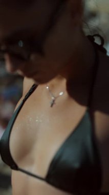 Canlı bir kadın plajda güneşin tadını çıkarıyor. Siyah bir bikini içinde, okyanus damlacıklarıyla parıldıyor.