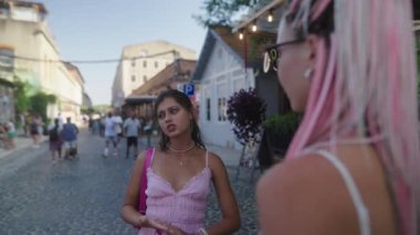 İki arkadaş, hareketli ve hareketli bir kaldırım taşı caddesinde neşeli ve hareketli bir sohbete girişiyor.