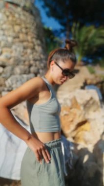 Şık, genç bir kadın, şık yaz kıyafetleri içinde, açık havada poz veriyor. Suyun güneşli gününün tadını çıkarıyor.