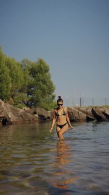 Genç bir kadın güneşli bir günde berrak sularda mutlu mesut yürürken huzurlu bir anın tadını çıkarıyor.