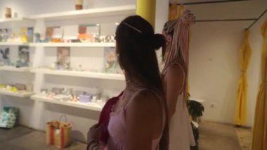 İki şık kadın, benzersiz dekorasyon ürünleri ve büyüleyici aksesuarlarla dolu bir moda dükkanını zevkle keşfederler.