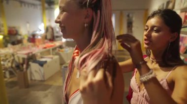 Çağdaş sanatla dolu canlı, yaratıcı bir mekanda, iki kadın stili ve birbirlerine güzel aksesuarlar takıyorlar.