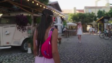 Cazibe ve neşe dolu hareketli bir açık hava pazarında iki yakın arkadaş mutlulukla kucaklaşır.