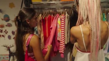 İki şık kadın şık bir butiği keşfediyor. Renkli kıyafetler ve modaya uygun kıyafetler sergiliyorlar.